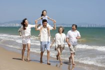 Fille chinoise sur les épaules du père marchant avec la famille sur la plage — Photo de stock