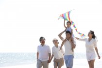 Китаянка с воздушным змеем на плечах отца гуляет с семьей на пляже — стоковое фото