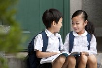 Китайский мальчик и девочка с книгой разговаривают на крыльце — стоковое фото