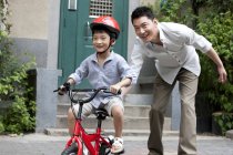 Padre chino entrenamiento hijo montar bicicleta - foto de stock
