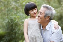Китайский дедушка и внучка обнимаются и смеются в саду — стоковое фото