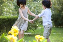 Chinese children holding hands and whirling in garden — Stock Photo