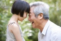 Chinese grandpa and granddaughter pressing foreheads in garden — Stock Photo