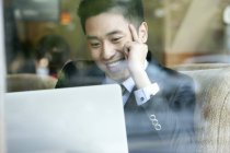 Homme d'affaires chinois utilisant un ordinateur portable dans un café et souriant — Photo de stock