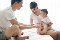 Chinese family with baby boy sitting on bed — Stock Photo
