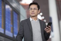 Asian man holding smartphone in airport — Stock Photo