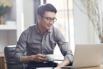 Hombre asiático trabajando con el ordenador portátil y café en la oficina - foto de stock