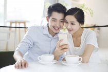 Coppia cinese utilizzando smartphone in caffetteria — Foto stock