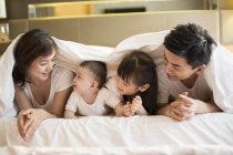 Família chinesa deitada na cama sob cobertor — Fotografia de Stock