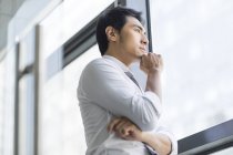 Замислений китайський бізнесмен дивлячись через вікно — стокове фото