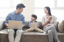 Familia china con niño usando aparatos digitales en el sofá - foto de stock