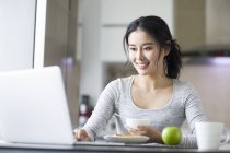 Mujer asiática usando el ordenador portátil mientras desayuna - foto de stock