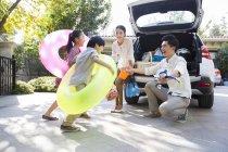 Chinois frères et sœurs portant des tubes de natation courir à la voiture avec les parents — Photo de stock