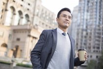 Китайский бизнесмен держит кофе и смотрит на город — стоковое фото
