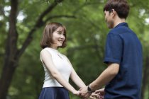Joven pareja china cogida de la mano en el parque - foto de stock