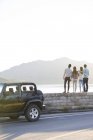 Vista posteriore di amici in piedi sul lungolago in periferia con auto — Foto stock