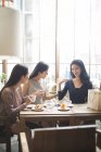 Mujer china demostrando ropa nueva a amigas en cafetería - foto de stock