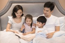 Китайський батьків і дітей, читаючи книгу в ліжку — стокове фото