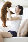Giovane donna cinese che gioca con barboncino animale domestico sul divano — Foto stock