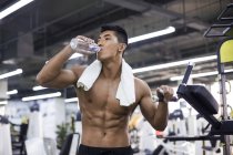 Hombre chino descansando y bebiendo agua en el gimnasio - foto de stock