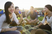 Chinese friends sitting on blanket at music festival and showing smartphone — Stock Photo