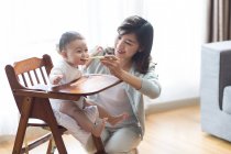 Chinês mãe alimentando bebê menino em cadeira alta — Fotografia de Stock