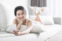 Asian woman using smartphone on sofa in home interior — Stock Photo