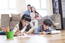 Asiatiques frères et sœurs étudiant ensemble à la maison tandis que les parents regardent — Photo de stock