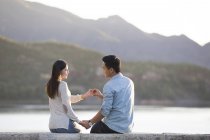 Chinese couple sitting on lakeside in suburbs and making love sign with hands — Stock Photo