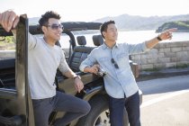 Chinese men leaning on car in suburbs and pointing — Stock Photo