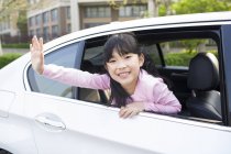 Asian girl leaning out of car window and waving — Stock Photo