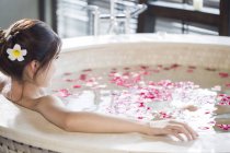 Young Chinese woman in bathtub with rose petals — Stock Photo