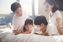 Genitori cinesi e bambini che leggono il libro a letto — Foto stock