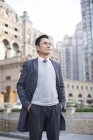 Chinese businessman standing with hands in pockets in city — Stock Photo