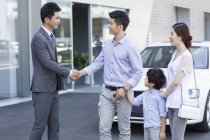 Família chinesa apertando as mãos com o vendedor de carros na frente do showroom — Fotografia de Stock