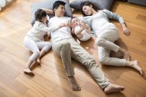 Familia china descansando en suelo de madera en la sala de estar - foto de stock