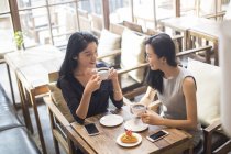 Китайские подруги пьют кофе и разговаривают в кафе — стоковое фото