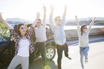 Chinese friends posing with arms raised in front of car — Stock Photo