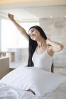 Chinese woman stretching in bed in morning and smiling — Stock Photo