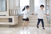 Chinesische Geschwister halten sich an den Händen und rennen im Wohnzimmer — Stockfoto