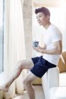 Uomo cinese che tiene il caffè e guarda attraverso la finestra a casa — Foto stock