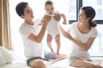 Chinese father and mother holding baby while sitting on bed — Stock Photo