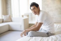 Chinese man sitting on bed and looking in camera — Stock Photo