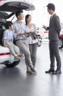Chinese family sitting in car trunk in showroom with car seller — Stock Photo