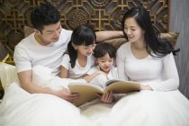 Asian parents reading book to children in bedroom — Stock Photo