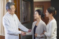 Зрілі китайський лікар вітають один одного з пацієнтом — стокове фото