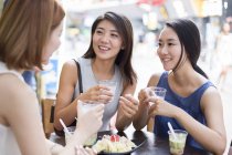 Женщины-друзья разговаривают и улыбаются в кафе на тротуаре — стоковое фото