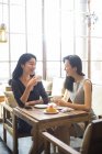 Chinese female friends drinking coffee and talking in cafe — Stock Photo