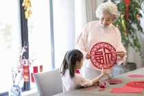 Granddaughter and grandmother making Chinese New Year paper-cut — Stock Photo