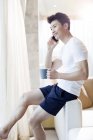 Hombre chino con café hablando por teléfono en casa - foto de stock
